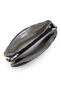 Kompakte navyblaue und weiße Muster-Kipling-Tasche mit zwei Hauptfächern und einer zentralen Reißverschlusstasche, geöffnet, um das hellgraue Innenfutter zu zeigen.