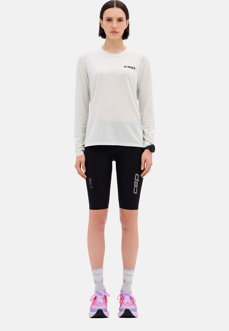 Long-sleeve light gray athletic shirt with black logo, paired with black knee-length shorts featuring white accents. Worn with pink and gray sneakers.