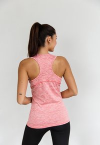 Roze, gestructureerde sporttanktop met racerback-ontwerp. Strak model met contrasterende naden en zijdetails, gecombineerd met zwarte leggings.