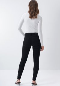 Černé skinny džíny s vysokým pasem, se dvěma zadními kapsami a hladkou texturou. Kombinované s bílým topem s dlouhým rukávem a žebrovanou strukturou.