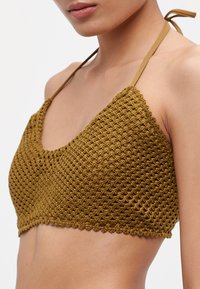 Olivengroene gehaakte bralette met driehoekige cups, gegolfde randen en dunne verstelbare bandjes. De textuur lijkt geweven en open gebreid.