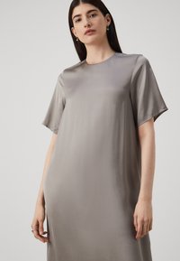 Rochie gri, asemănătoare mătăsii, cu mâneci scurte, guler rotund și croială lejeră. O strălucire subtilă și o textură fină accentuează designul său minimalist.