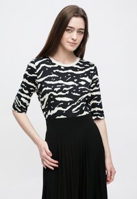 Mustvalge sebratriibuline topp, millel on ümmargune kaelus ja kolmveerandvarrukad, kombineeritud volditud musta seelikuga. Sile tekstuur.