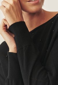 Schwarzer Pullover mit strukturiertem Muster und Perlenakzenten, mit gerippten Bündchen und entspannter Passform, der aus einem weichen Strickstoff besteht.