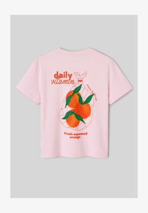 T-shirt rose avec graphique au dos de trois oranges dans un filet, feuilles vertes, et texte orange : « vitamine quotidienne », « pressé par le soleil », « orange fraîchement pressée ».