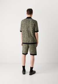 Short-sleeve shirt and shorts set in patterned green fabric with black accents and trim; features a textured design and relaxed fit.