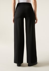 Pantalons larges noirs en tissu doux avec un design taille haute. Présentent un ourlet lisse et sans couture, ainsi qu'une esthétique minimaliste.