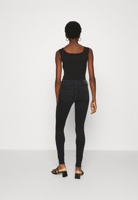 Top negro sin mangas combinado con unos jeans de mezclilla oscuros y ajustados. La modelo lleva sandalias negras con tiras. Texturas suaves, detalles mínimos.