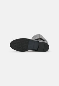 Stivale in pelle nera al ginocchio con suola in gomma testurizzata e dettaglio con zip lungo il lato, che mette in risalto un design slanciato.