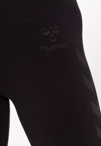 Czarne legginsy z fakturowanym wykończeniem, nadrukowanym logo oraz geometrycznym wzorem po boku. Materiał zdaje się być elastyczny i dopasowany do sylwetki.