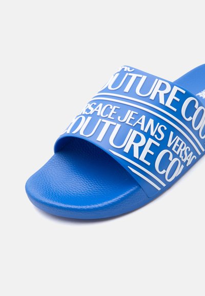 Синя слайд сандала с релефна подметка и широка каишка с изпъкнало бяло лого "Versace Jeans Couture" с удебелени букви.