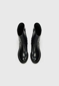Botas de tobillo de cuero negro con textura lisa, puntera redonda y cremallera lateral. Cuentan con una suela robusta con detalles de costura en contraste.