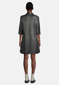 Abito in pelle nera con design sartoriale, maniche a metà, e linea dritta, caratterizzato da una texture liscia e minimi dettagli in metallo.