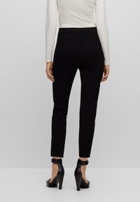 Zwarte, slimfit broek met een gladde textuur, voorzien van een hoge tailleband en een enkel-lange snit, gecombineerd met zwarte hoge hakken.