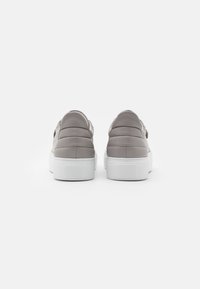 Scarpe slip-on grigie imbottite con una tomaia liscia, suole in gomma bianche e design minimalista, caratterizzate da una punta arrotondata e senza hardware visibile.