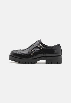 Chaussure brogue en cuir noir avec double boucle, détails perforés, bout arrondi et semelle robuste pour une meilleure adhérence et durabilité.
