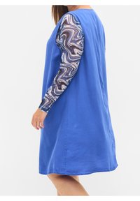 Blå klänning med avslappnad passform och långa, mönstrade ärmar med virvlar av brunt och blått. Slät textur, knä-lång design.