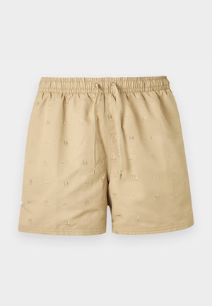 Beige shorts med elastisk midje og snor, med små broderte logoer og "12"-mønstre jevnt fordelt på stoffet.