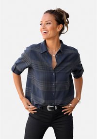 Navy plaid button-up shirt in soft fabric, features roll-up sleeves, chest pocket, and a relaxed fit, paired with black pants and accessories.
