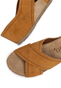 Brown suede sandals with crisscross straps, open toe design, and textured inner sole. Features subtle stitching and logo imprint.