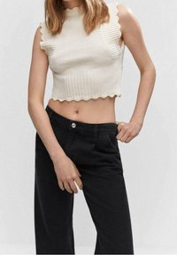 Top corto blanco de canalé con bordes ondulados, combinado con pantalones negros de cintura alta. La textura de la tela es suave y ajustada.