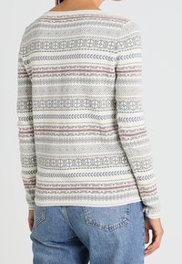 Suéter de manga larga con un patrón geométrico en gris, rosa y azul marino sobre un fondo crema; textura de punto suave y escote redondo.