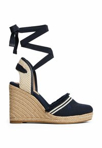 Navy wedge espadrille with a woven jute sole, fabric upper, striped accents, and crisscross ankle straps. Textured side panel in woven material.
