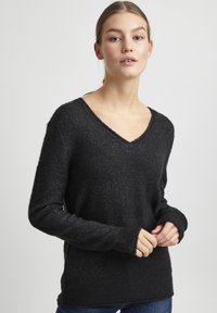 Pull noir à manches longues avec un design en V, motif en maille texturé et coupe légèrement ample. Détails de bord-côtes aux poignets et à l'ourlet.