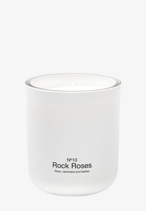 Bougie blanche dans un récipient en céramique lisse étiqueté "N°10 Rock Roses" avec des notes de parfum de rose, cachemire et cuir.