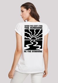 White cotton t-shirt with short sleeves, featuring a black graphic design on the back with a sun and text "When you can't find the sunshine, be the sunshine."
