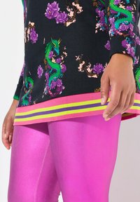 Felpa nera con vivaci motivi di drago e floreali, abbinata a leggins rosa lucidi. Presenta un orlo a righe colorate.
