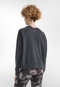 Felpa grigio scuro con maniche raglan, caratterizzata da una piccola etichetta viola sul retro. Texture morbida. Abbinata a leggings con motivo.