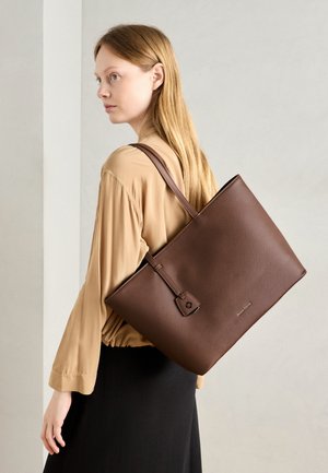 Sac fourre-tout marron en matériau texturé avec une forme plate, une poignée sécurisée et une petite étiquette décorative. Porté à l'épaule sur un fond neutre.