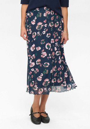 Mittel-lange marineblaue Rock aus leichtem Stoff, mit einem floralen Muster in Pink und Grün, mit einem gewellten Saum. Getragen mit schwarzen Schuhen.