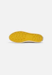 Semelle en caoutchouc jaune d'une chaussure avec motif antidérapant texturé visible sur fond blanc uni.