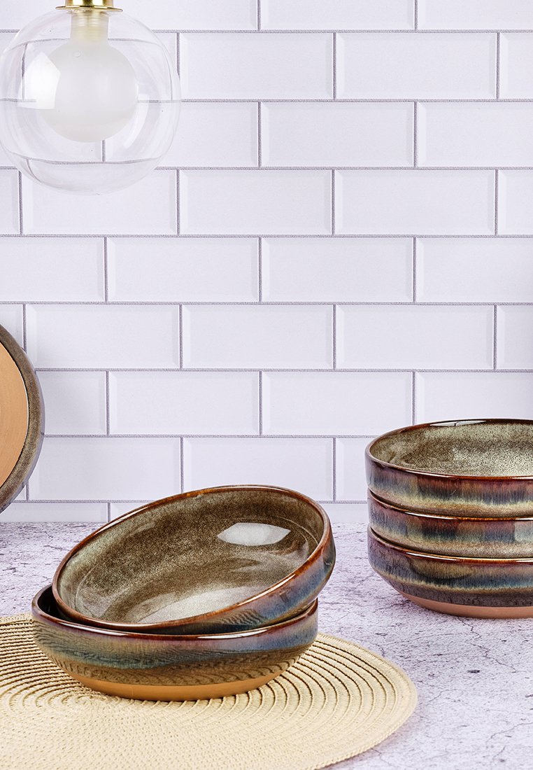 Handgefertigte Keramikteller mit einer glänzenden braunen und türkisfarbenen Oberfläche, mit strukturierten Kanten und glatten Innenseiten, auf einem runden Tischset gestapelt.