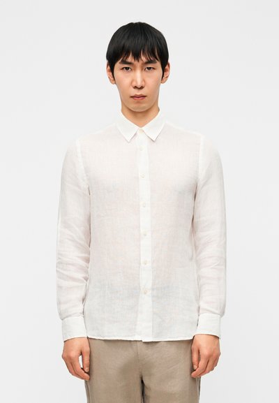 Chemise blanche à manches longues en lin léger avec un col boutonné et une patte de boutonnage, présentant une texture légèrement transparente.