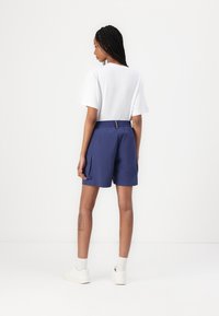 Navy blue shorts with an elastic waistband, featuring side pockets and a visible yellow zipper accent, paired with a white t-shirt.