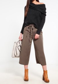 Maglione lavorato a maglia nero con spalle scoperte, pantaloni beige a gamba larga con cintura regolabile, stivali alla caviglia marroni e borsa a tracolla grigia chiara. Texture lisce.