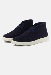 Botas de ante en color marino hasta el tobillo con punta redondeada, presentan cordones azules y una suela de goma blanca. Detalle de costura sutil en la parte superior.