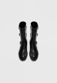 Botas negras hasta la rodilla con un acabado de cuero suave, que cuentan con tres hebillas doradas, una puntera redondeada y una suela resistente para ofrecer agarre.