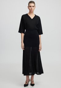 Top nero a maglia con scollo a V e maniche ampie abbinato a una gonna nera knee-length con pannelli trasparenti, completato da tacchi a spillo neri.