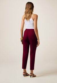 Bordeaux elastische taillebandbroeken met taps toelopende pijpen en een gladde textuur, gecombineerd met een witte tanktop en zwarte hoge sandalen.