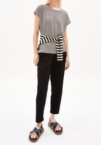 Paskowy czarno-biały top z krótkim rękawem, związany czarno-białym paskiem w paski, połączony z czarnymi zwężającymi się spodniami i czarnymi sandałami z drewnianą podeszwą.