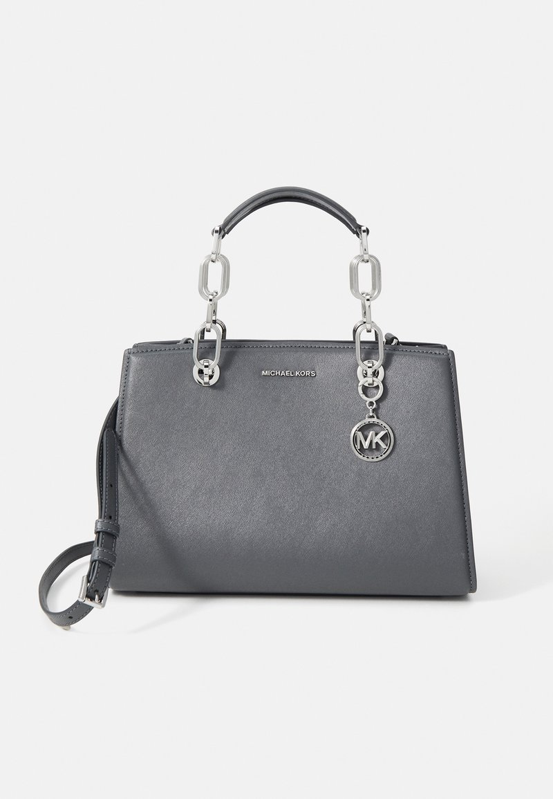 Sac à main gris Michael Kors avec poignées en chaîne argentée, bandoulière détachable et pendentif rond avec logo MK à l'avant.