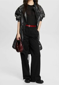 Giacca impermeabile nera, oversize, top in maglia nera aderente, pantaloni neri a gamba larga, cintura rossa, borsa bordeaux, scarpe nere chunky.