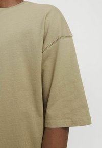 Camiseta de algodón khaki de manga corta con cuello redondo. Presenta un ajuste relajado y costuras limpias en las mangas y el dobladillo. Textura suave.