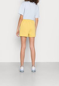 T-shirt bleu clair à manches courtes et coupe décontractée associée à un short en coton jaune. Le short possède une ceinture élastique et une texture lisse.