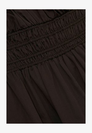 Brūns audums ar savilktām elastīgām detaļām jostasvietā un plūstošām krokām zemāk. Mīksta tekstūra un viegla izskata.