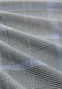 Katoenen stof met een gestructureerd oppervlak, met een patroon van kleine vierkanten en strepen in grijs, marineblauw en lichtblauwe tinten.